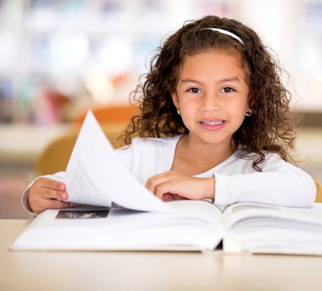 Happy girl reading a book at the school library